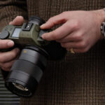 a person in a brown tweed coat holds a green leica camera 660x371 1